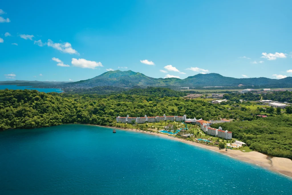 Aerial view of Dreams Playa Bonita Panama nestled along a secluded beach, surrounded by lush rainforest and mountain landscapes.