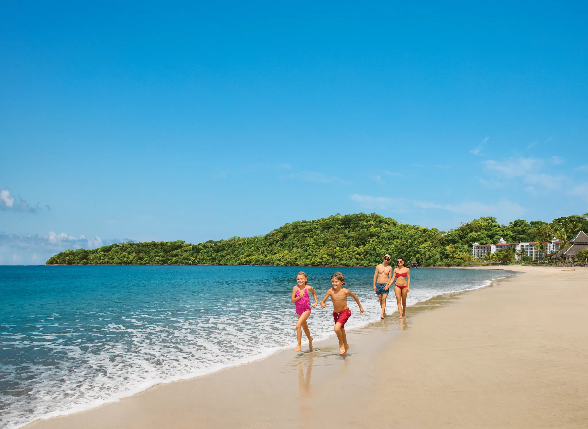 Family enjoying a beach walk along the shoreline at Dreams Playa Bonita Panama, with calm waters and lush tropical scenery.