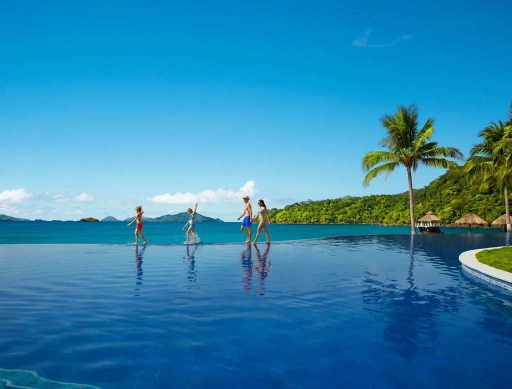 Family walking and playing in the infinity pool overlooking the ocean at Dreams Playa Bonita Panama, surrounded by lush tropical scenery.