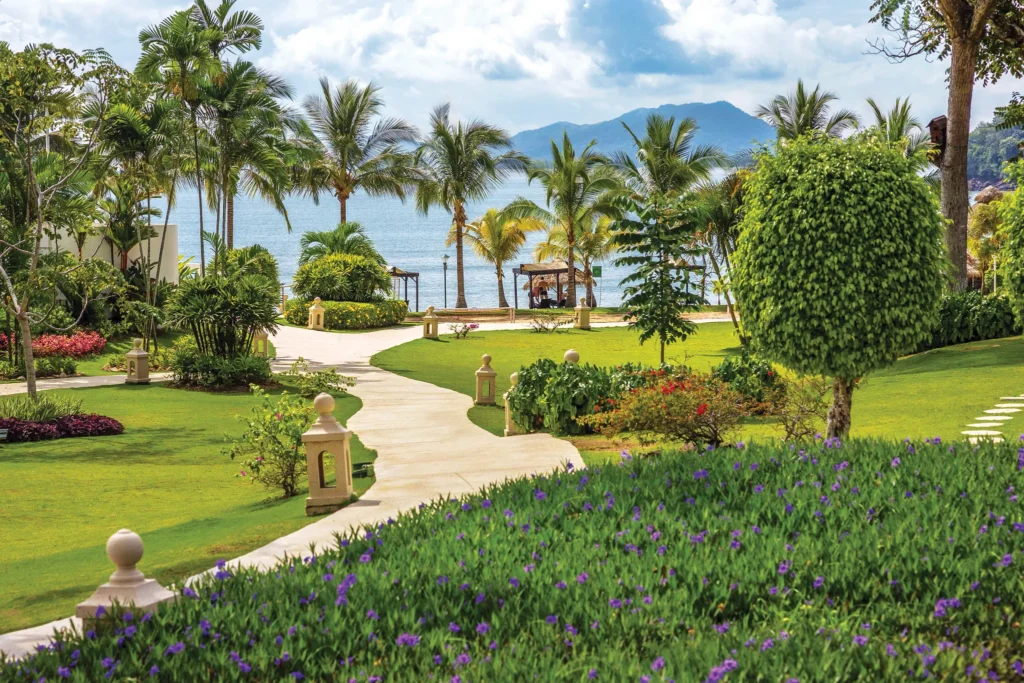 Tropical garden pathways leading to the beach at Dreams Playa Bonita Panama, surrounded by palm trees, ocean views, and lush greenery.