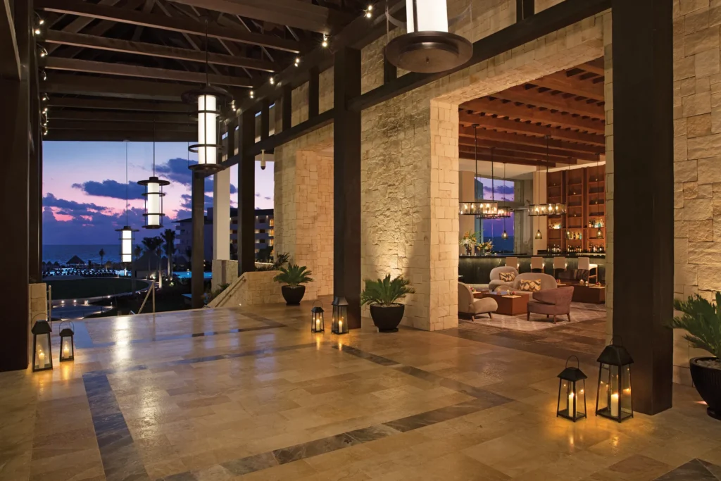Open-air lobby with warm lighting and ocean views at Dreams Playa Mujeres Resort at sunset.