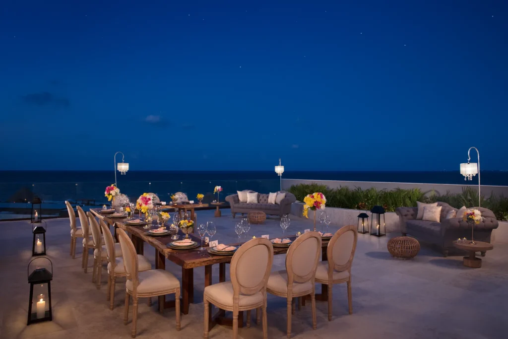 Outdoor terrace set for dinner with ocean view at night.