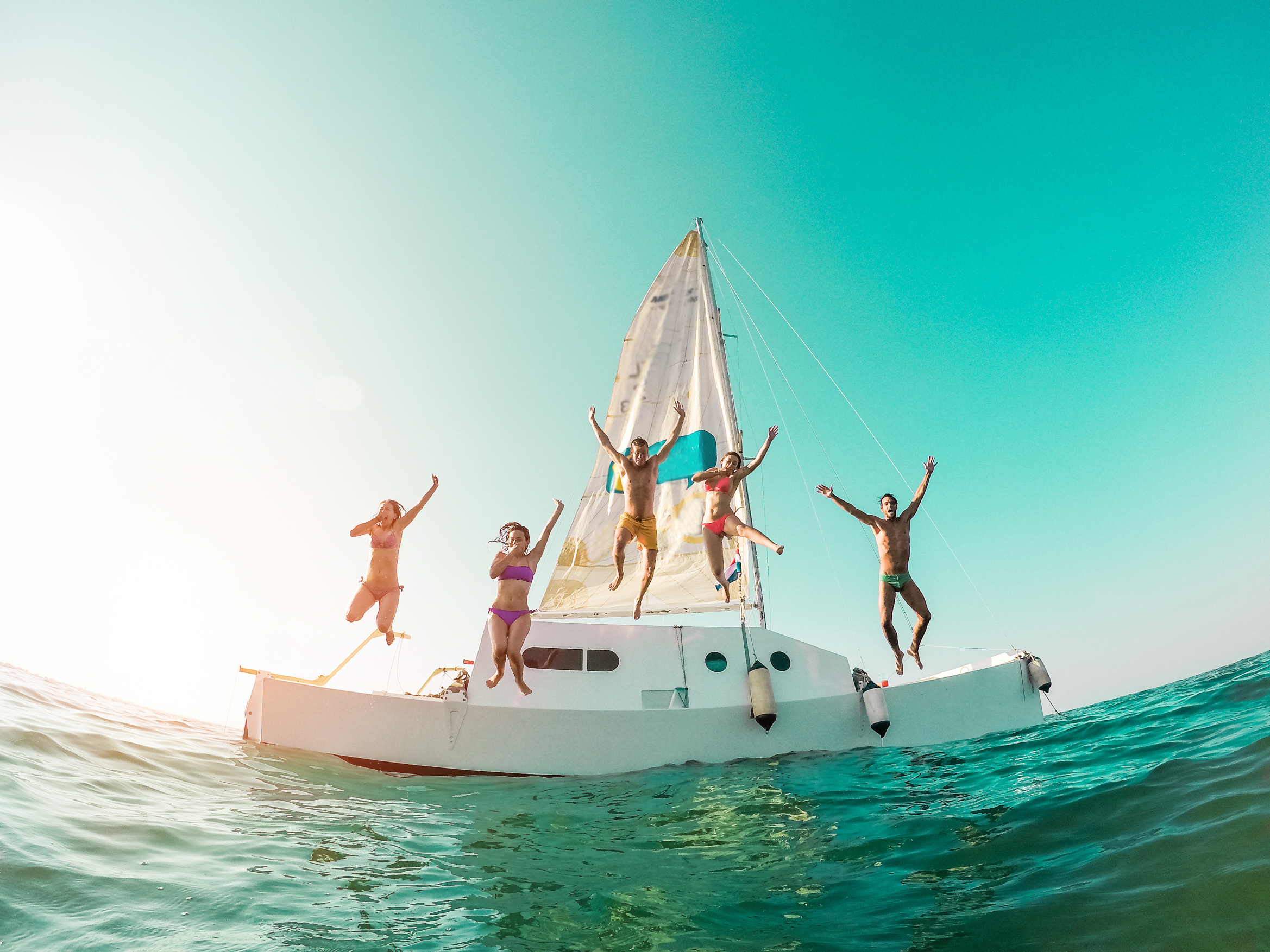 Happy crazy friends diving from sailing boat into the sea