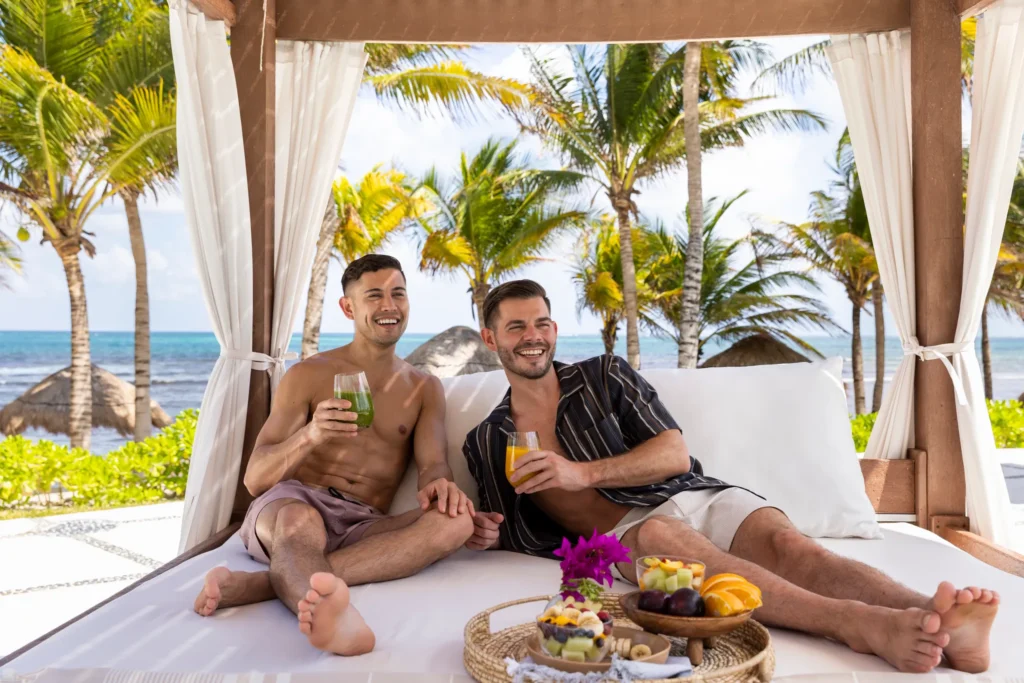 Two guests relaxing in a beachfront cabana with smoothies and ocean views.