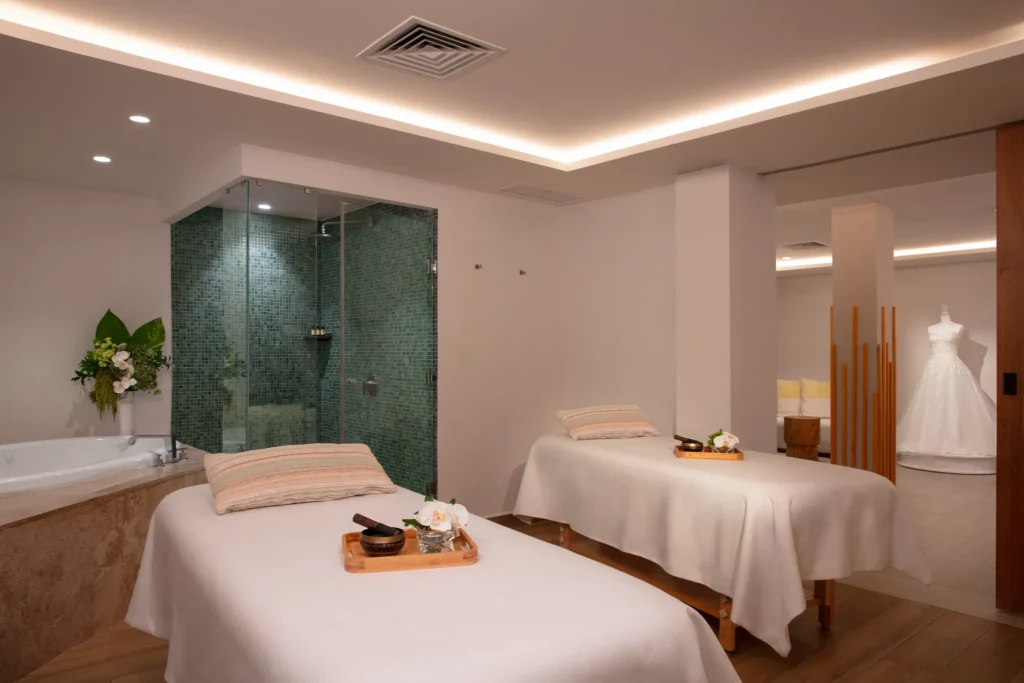 Elegant spa treatment room with two massage tables, bathtub, and glass shower.