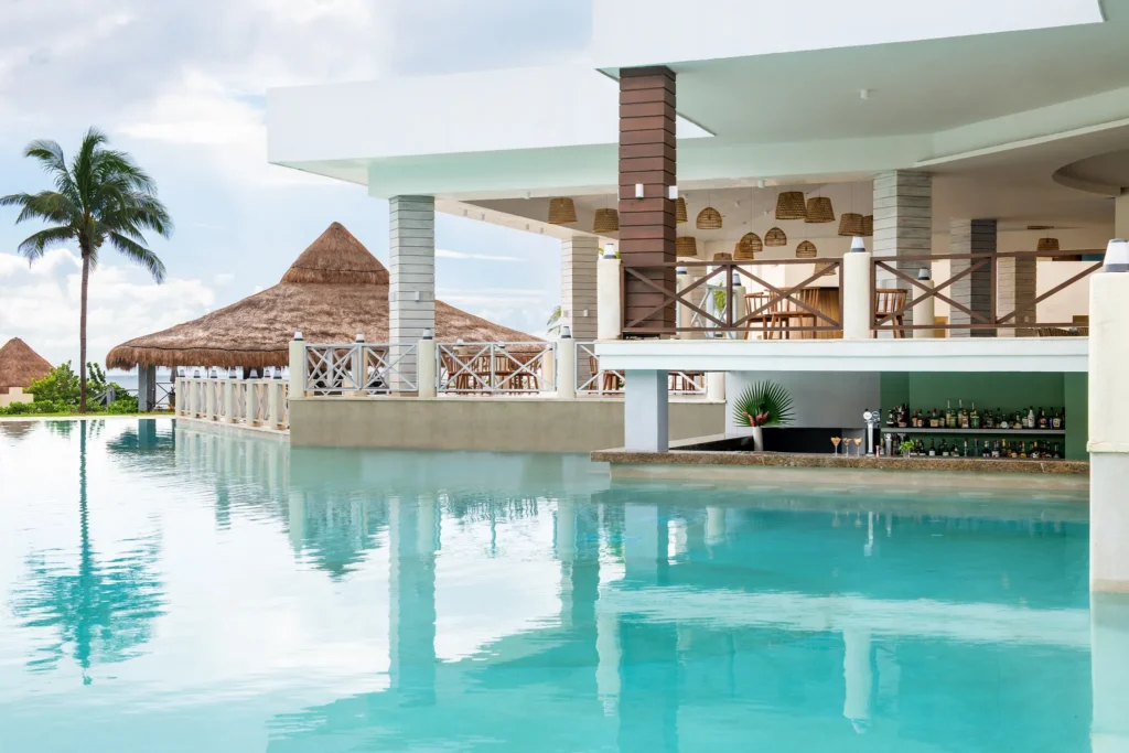 Delfin swim-up bar at Dreams Puerto Morelos Resort & Spa featuring a main pool bar, submerged seating, and tropical oceanfront surroundings.