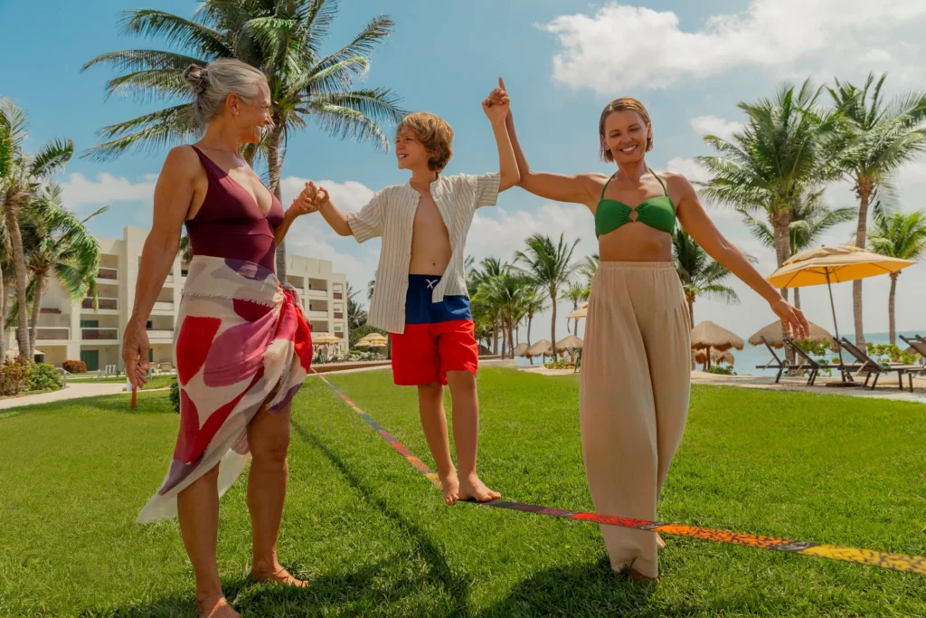 Family walking together on a lawn near the beach and palm trees at Dreams Puerto Morelos Resort & Spa.