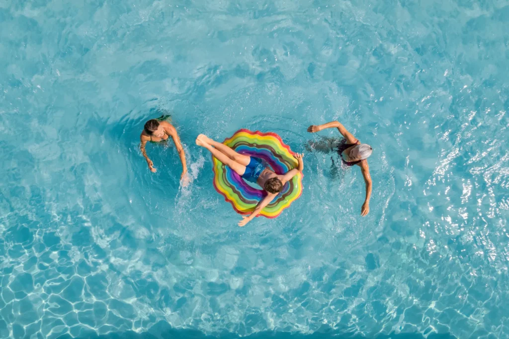 Child relaxing on a rainbow float while family swims in a clear blue pool at Dreams Puerto Morelos Resort & Spa.
