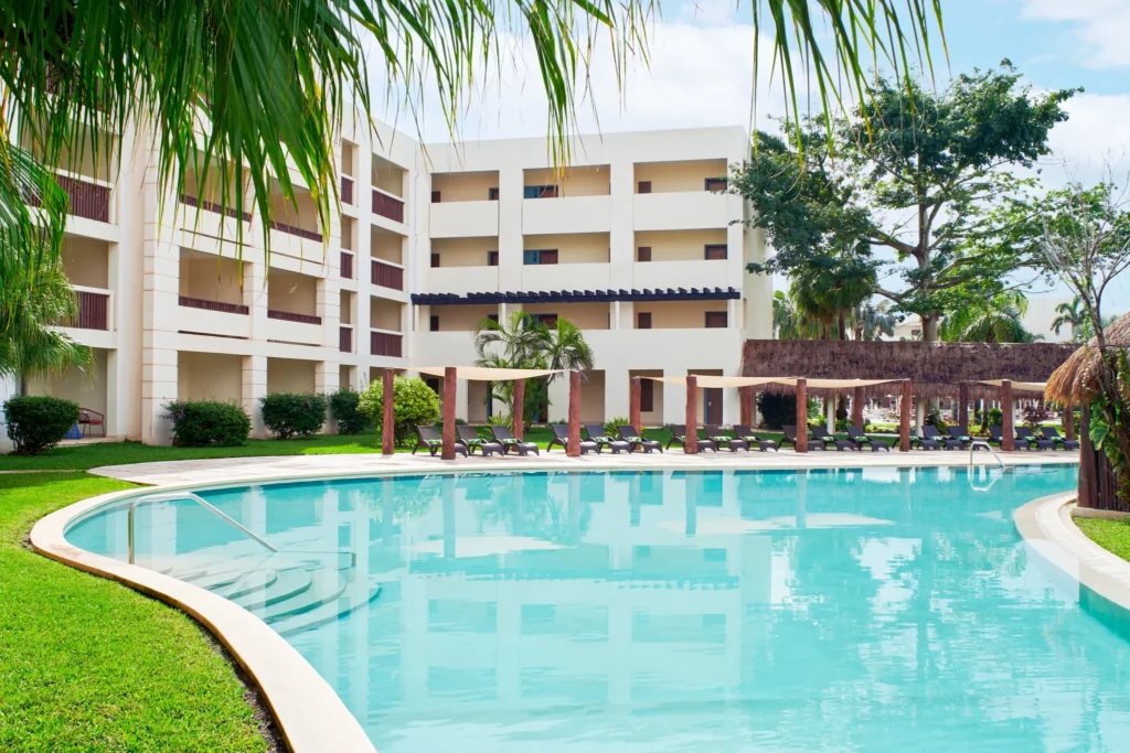 Quiet resort pool surrounded by greenery and lounge chairs near guest buildings.