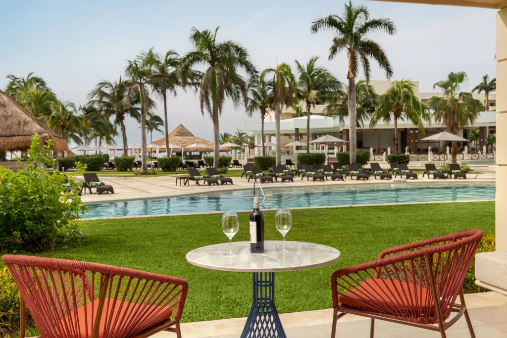 Junior Suite Pool View King balcony with seating overlooking pool and palm trees at Dreams Puerto Morelos Resort.