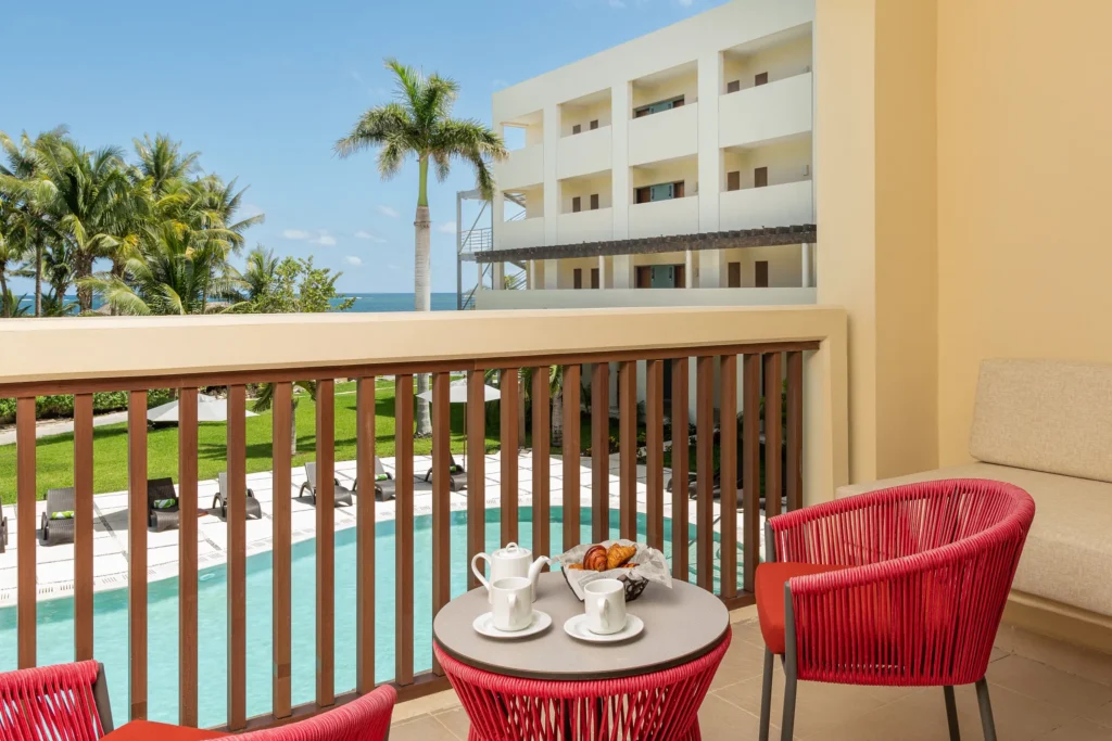 Junior Suite Tropical View balcony with seating area overlooking pool and tropical gardens at Dreams Puerto Morelos Resort.