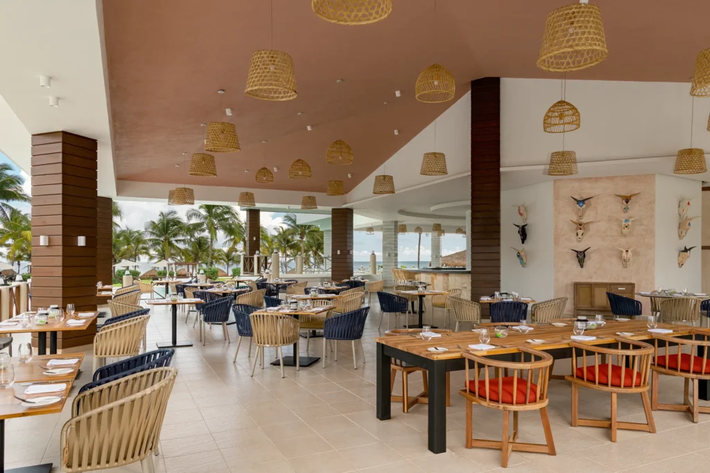La Parrilla open-fire grill restaurant at Dreams Puerto Morelos Resort & Spa featuring open-air dining, wood accents, and tropical ocean views.