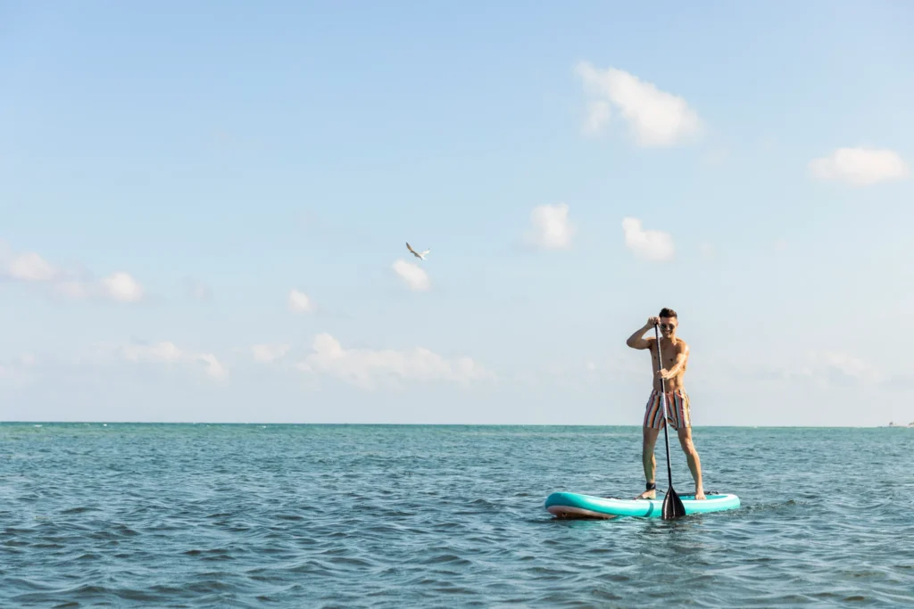 Man paddleboarding on calm ocean waters near the beach at Dreams Puerto Morelos Resort & Spa.