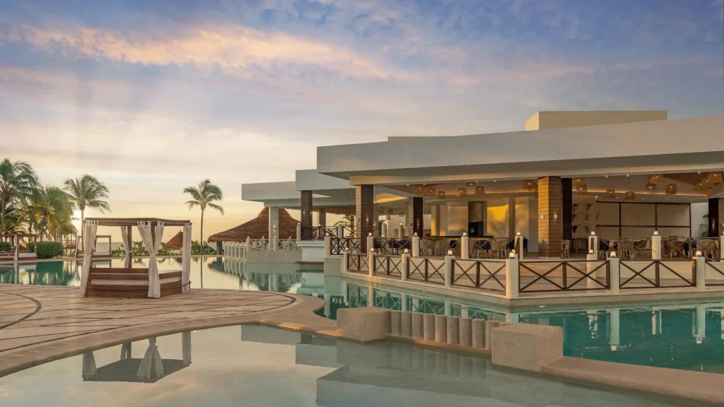 Resort pool and restaurant area at sunset at Dreams Puerto Morelos Resort & Spa.