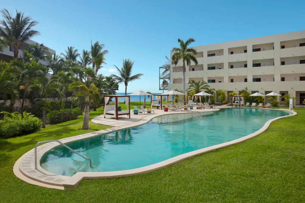 Curved resort pool surrounded by palm trees and loungers at Dreams Puerto Morelos Resort & Spa.