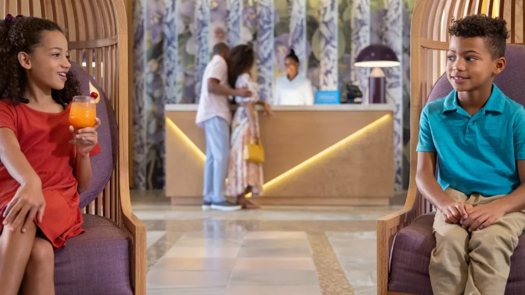 Children relaxing in the lobby at Dreams Rose Hall Resort & Spa while families check in for a Caribbean vacation in Jamaica.