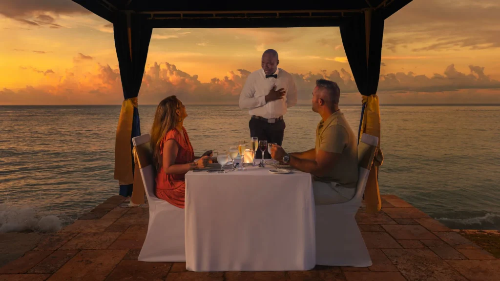 Couple enjoying a romantic sunset dinner by the ocean at Dreams Rose Hall Resort & Spa in Montego Bay, Jamaica.