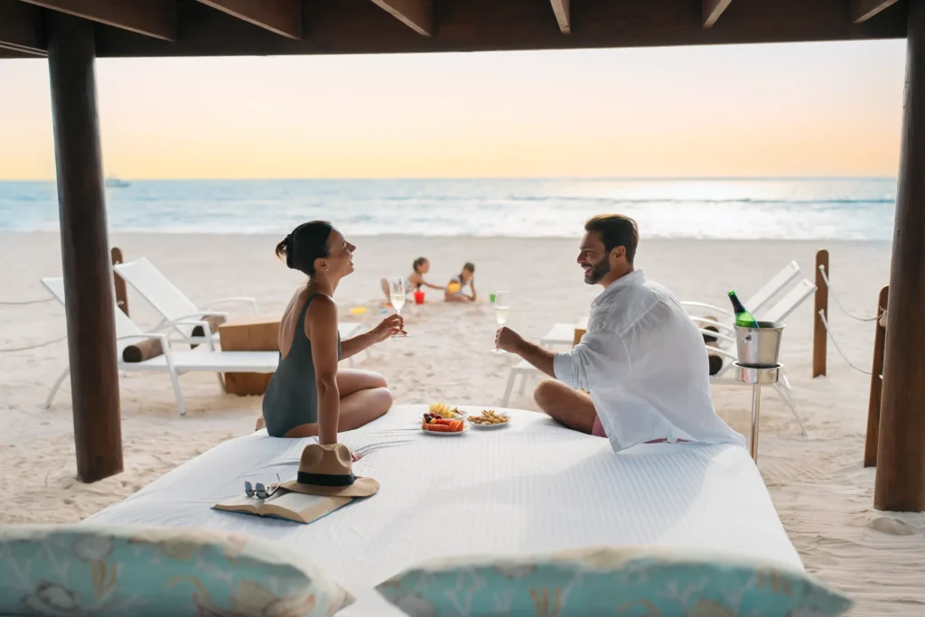 Couple enjoying champagne on a private beach setup at Dreams Royal Beach Punta Cana while children play nearby.