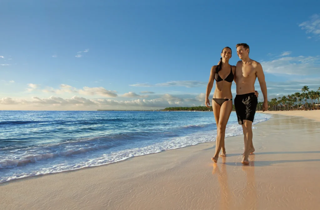 Couple walking along the shoreline at Dreams Royal Beach Punta Cana during golden hour.
