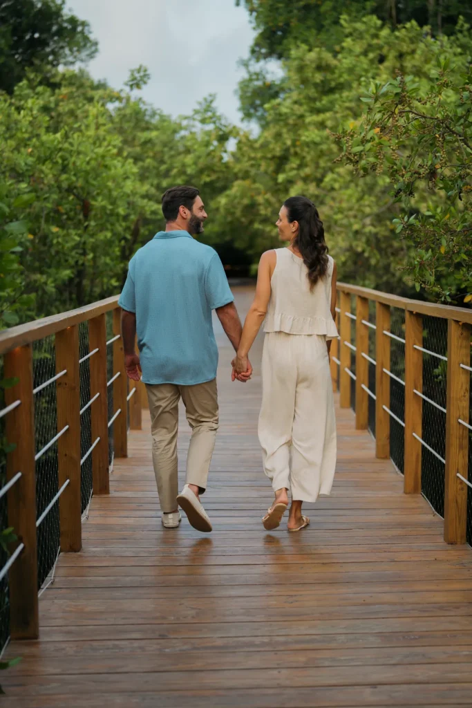Couple holding hands walking along a wooden pathway surrounded by lush greenery at Dreams Royal Beach Punta Cana.