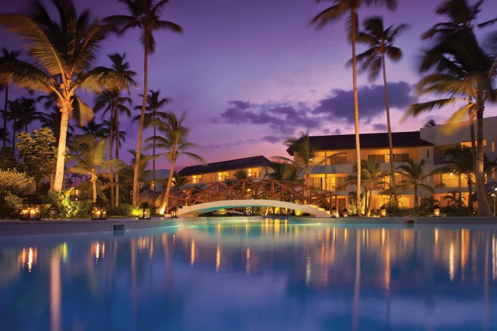 Illuminated pool with bridge and palm trees at sunset at Dreams Royal Beach Punta Cana.