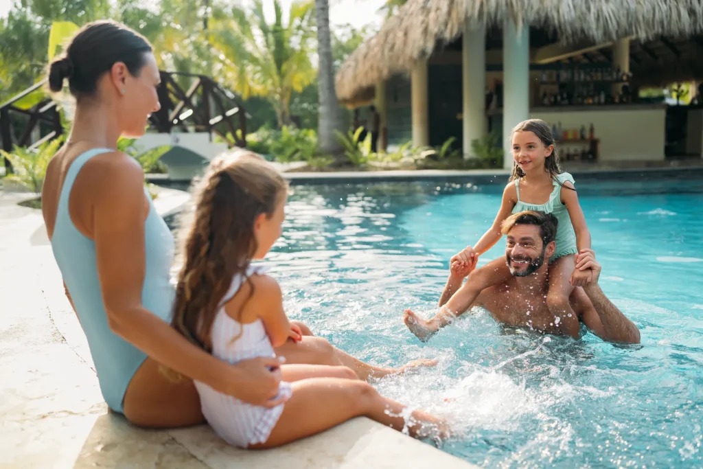 Family enjoying a refreshing swim in a tropical pool at Dreams Royal Beach Punta Cana surrounded by lush greenery.