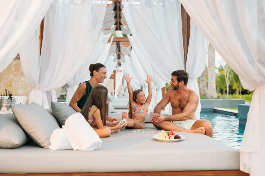 Family spending quality time together on a shaded Bali bed at Dreams Royal Beach Punta Cana surrounded by lush tropical scenery.