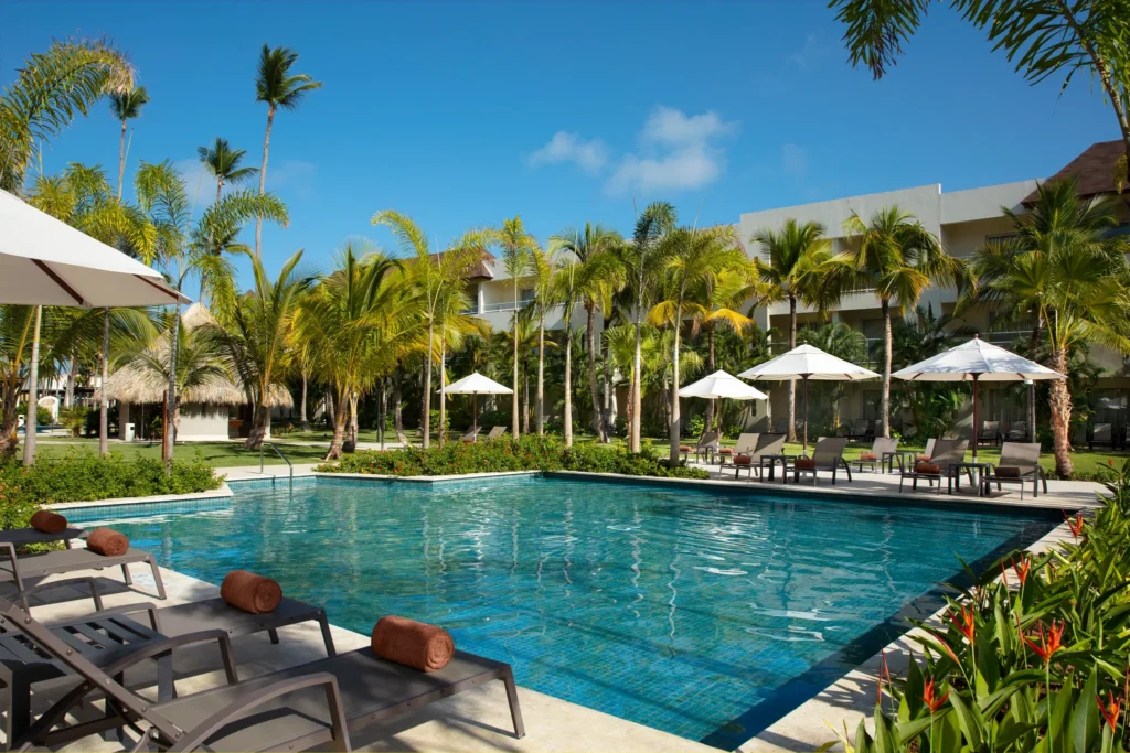 Relaxing pool area with lounge chairs and umbrellas surrounded by palm trees at Dreams Royal Beach Punta Cana.