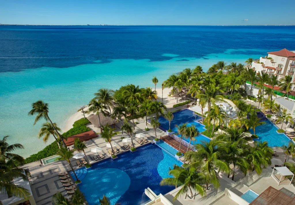 Aerial view of pools, palm trees, and turquoise Caribbean waters at Dreams Sands Cancun Resort & Spa.