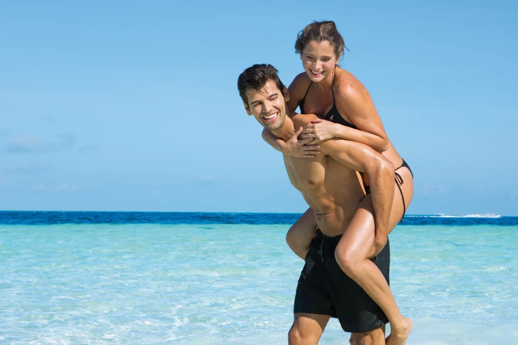 Couple enjoying a playful piggyback ride in shallow Caribbean waters at Dreams Sands Cancun Resort & Spa.