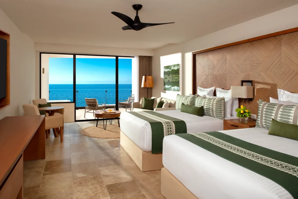 Club Junior Suite Ocean Front with two double beds and private balcony overlooking the Caribbean Sea at Dreams Sapphire Resort & Spa.