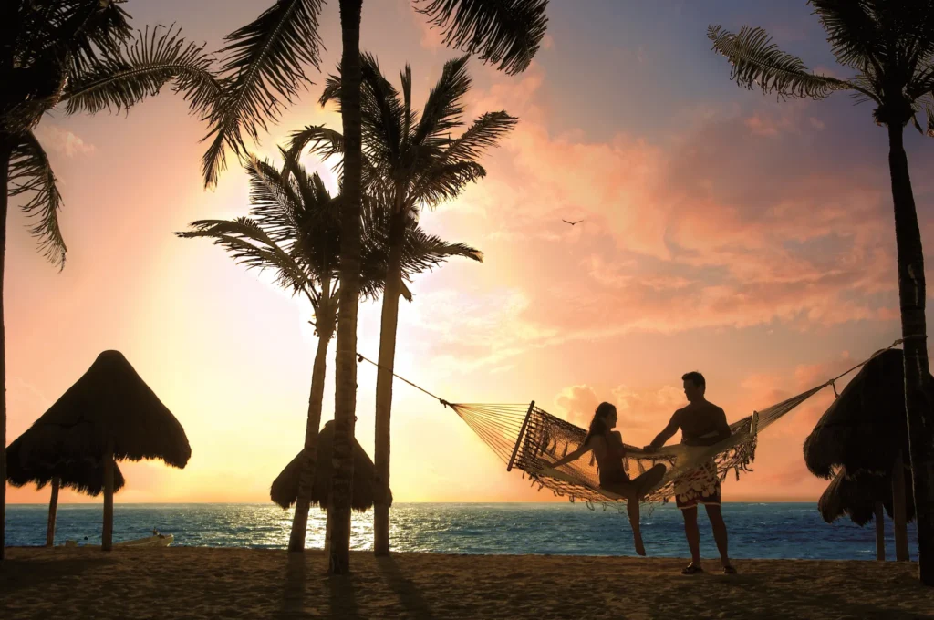 Couple relaxing in a hammock at sunset on the beach at Dreams Tulum Resort & Spa in Riviera Maya.