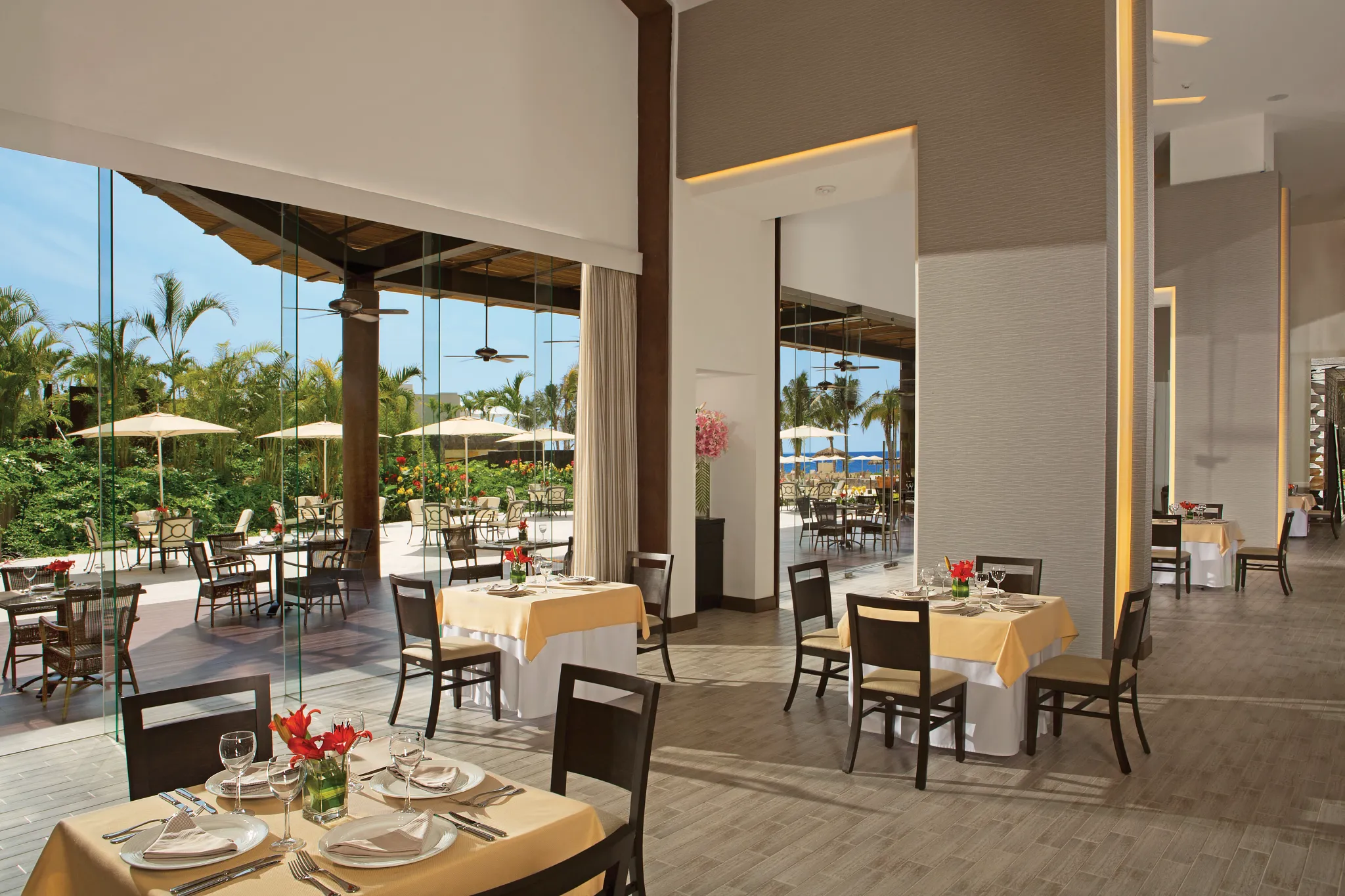Carnival buffet restaurant at Dreams Vallarta Bay Resort & Spa with modern dining room, floor-to-ceiling windows, and outdoor terrace seating overlooking tropical gardens.