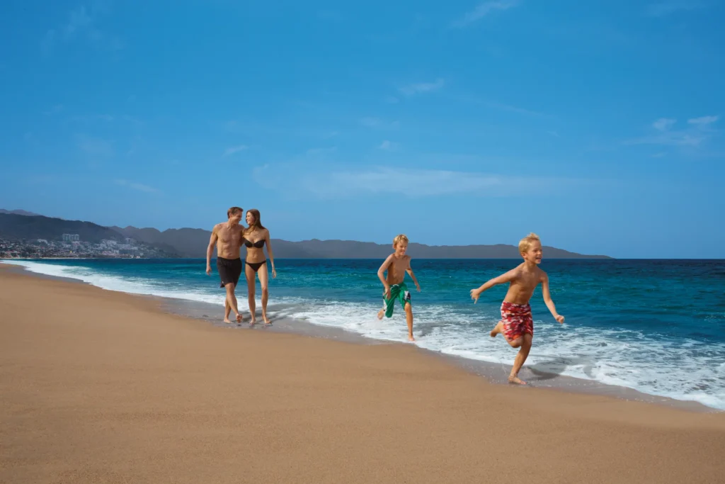 Parents and children running and playing along the beach at Dreams Vallarta Bay Resort & Spa.
