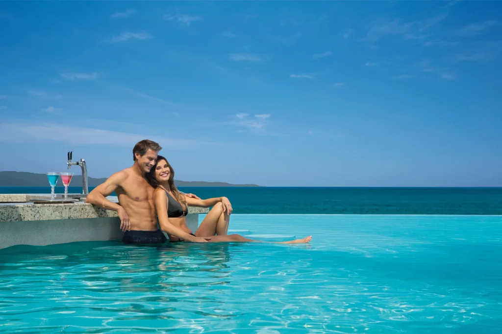 Couple relaxing in the infinity pool with tropical cocktails at Dreams Vallarta Bay Resort & Spa pool bar.