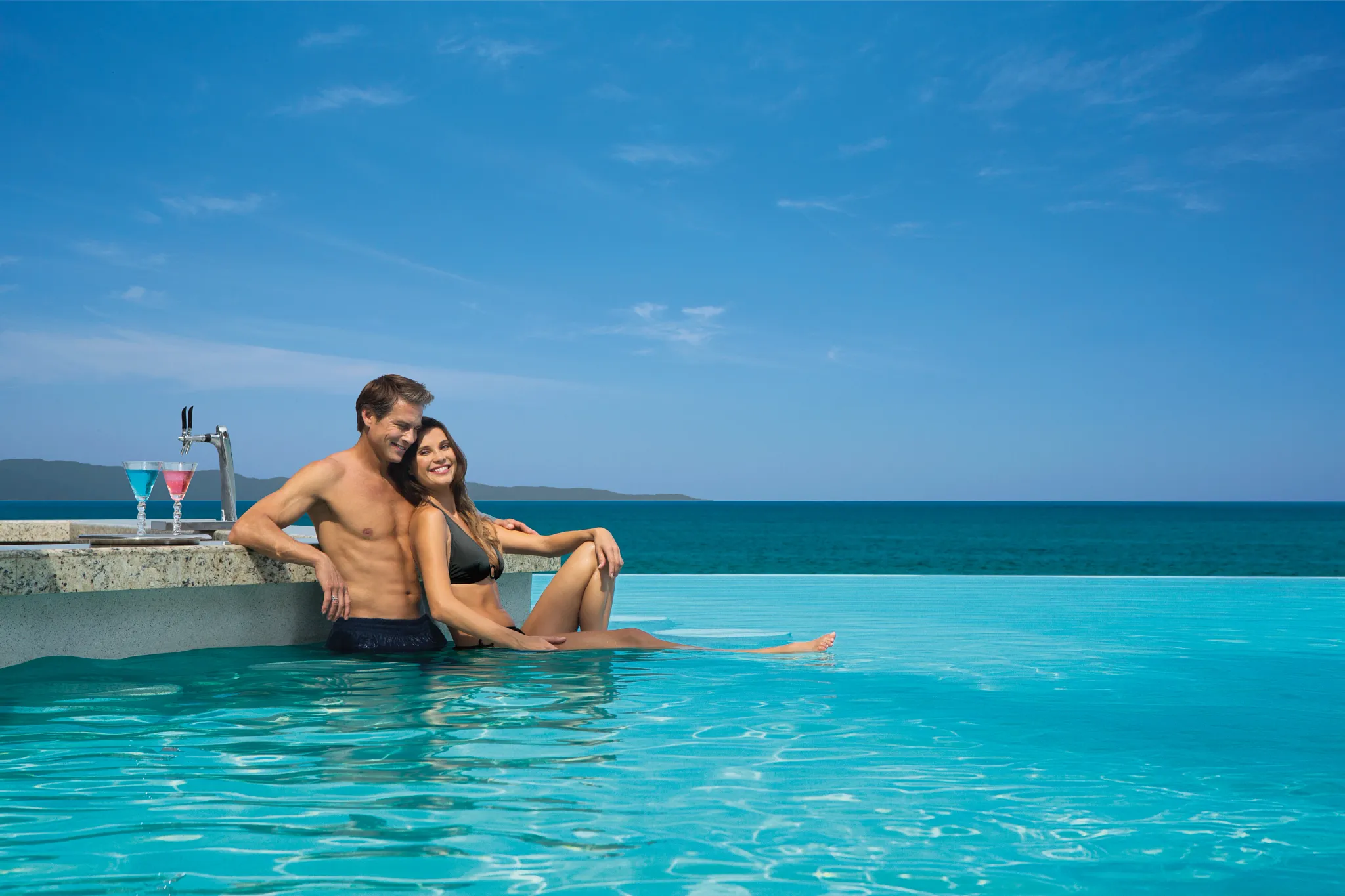 Couple relaxing in the infinity pool with tropical cocktails at Dreams Vallarta Bay Resort & Spa pool bar.