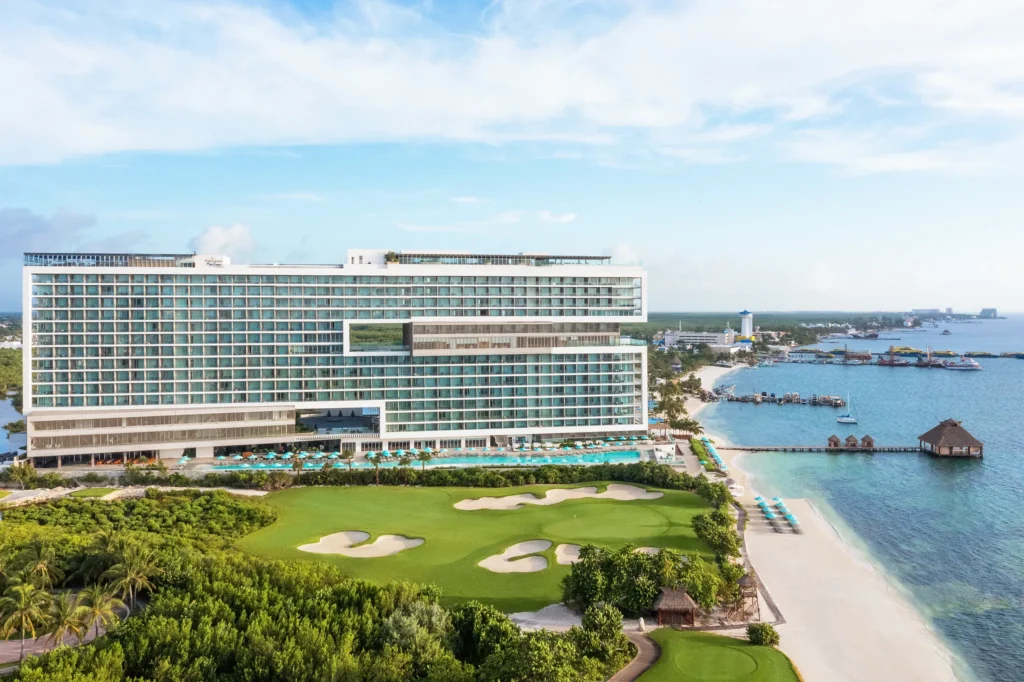 Luxury resort building and beach at Dreams Vista Cancun Golf & Spa Resort overlooking clear blue water.