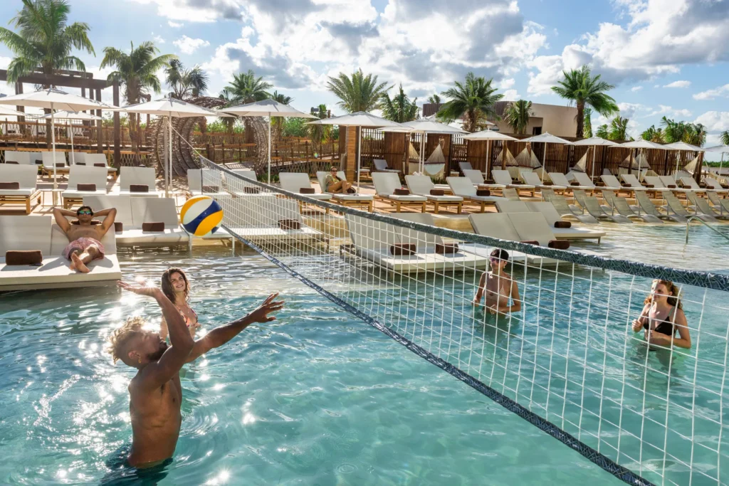 Guests playing water volleyball in a pool at Hyatt Vivid Grand Island with loungers and cabanas in the background.
