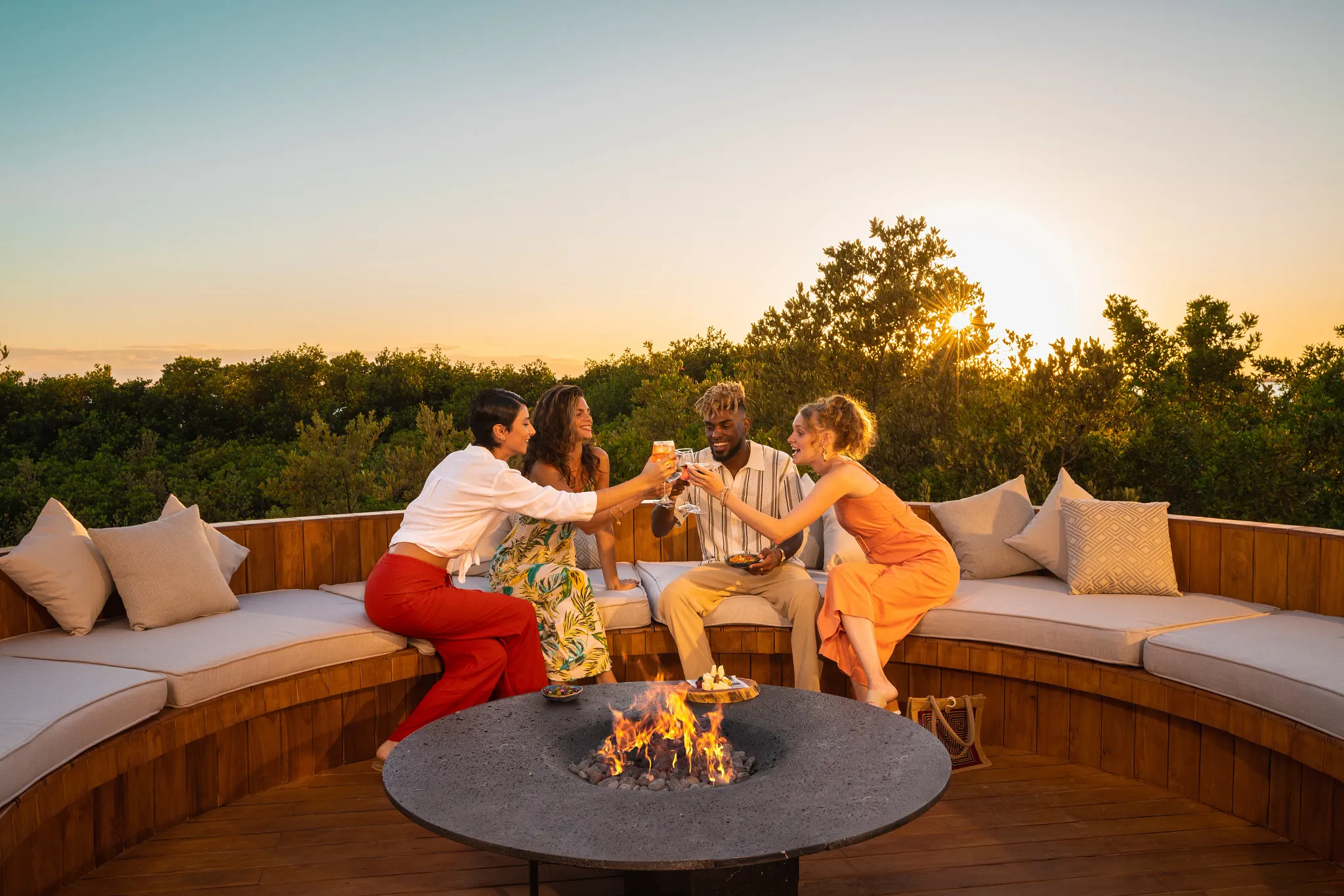 Friends enjoying drinks around a fire pit at sunset at Hyatt Vivid Grand Island outdoor lounge.