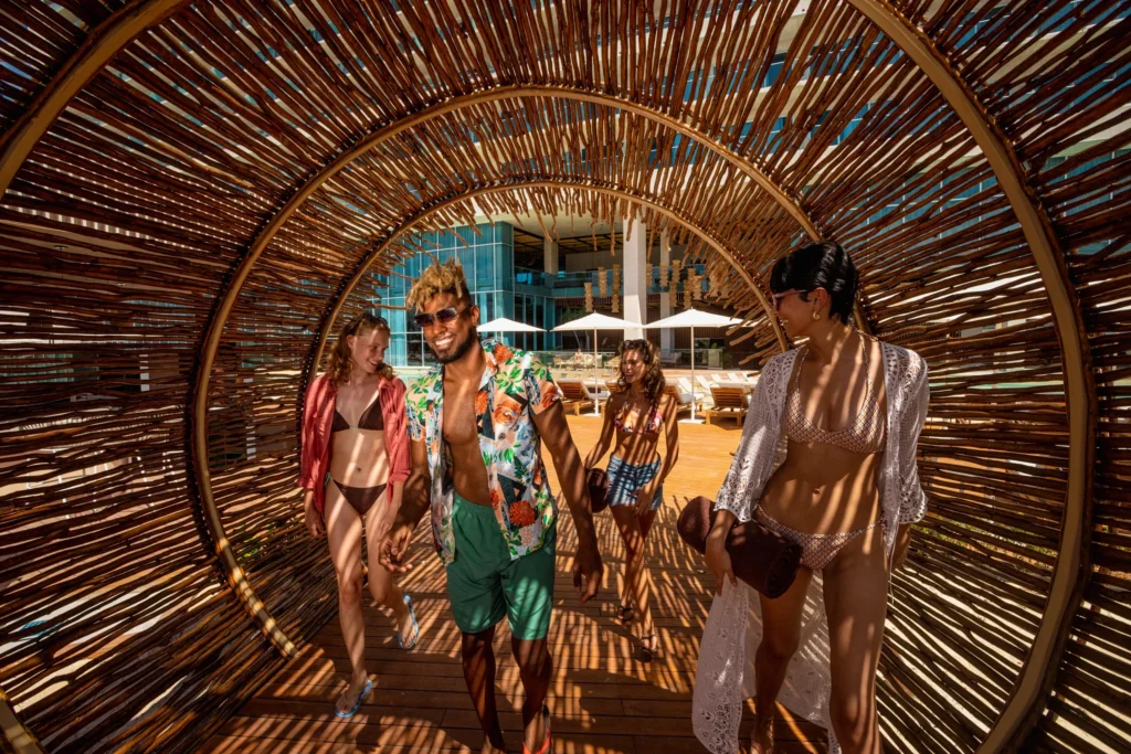 Friends walking through a woven tunnel walkway toward the pool area at Hyatt Vivid Grand Island in Cancun.