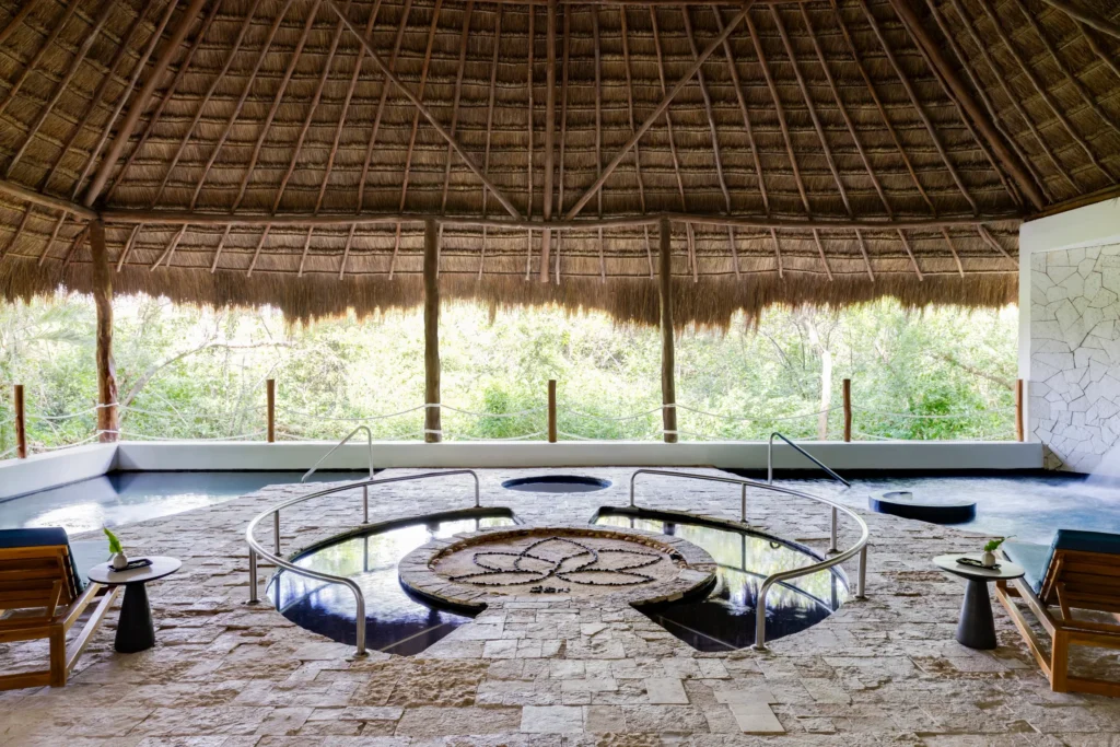 Open-air hydrotherapy pool under a thatched roof surrounded by lush jungle at Hyatt Zilara Riviera Maya spa.