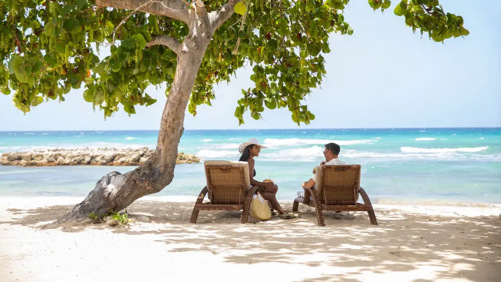Couple relaxing in lounge chairs beneath a shade tree overlooking the Caribbean Sea at Hyatt Zilara Rose Hall.