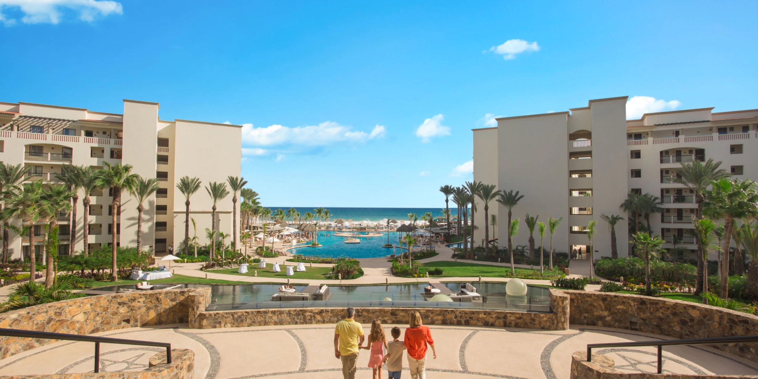 Family walking through Hyatt Ziva Los Cabos with oceanfront pools, tropical gardens, and beachfront views.