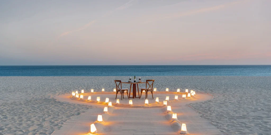 Private candlelit dinner setup on the beach at Hyatt Ziva Los Cabos during sunset.