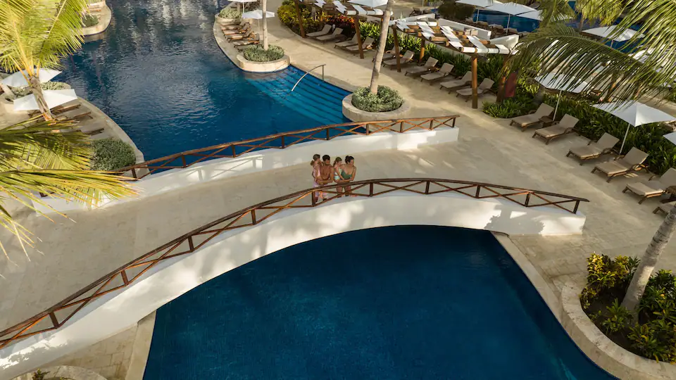 Guests walking across a bridge overlooking the lagoon-style pools at Hyatt Ziva Cap Cana, surrounded by tropical landscaping and luxury amenities.