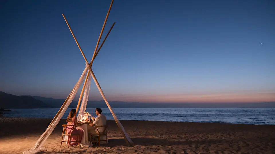 Couple enjoying an intimate candlelit dinner on the beach at Hyatt Ziva Puerto Vallarta at twilight.