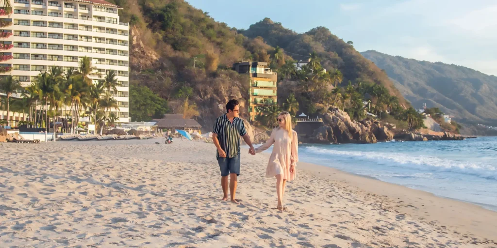Couple holding hands while walking along the sandy beach at Hyatt Ziva Puerto Vallarta during a romantic getaway.