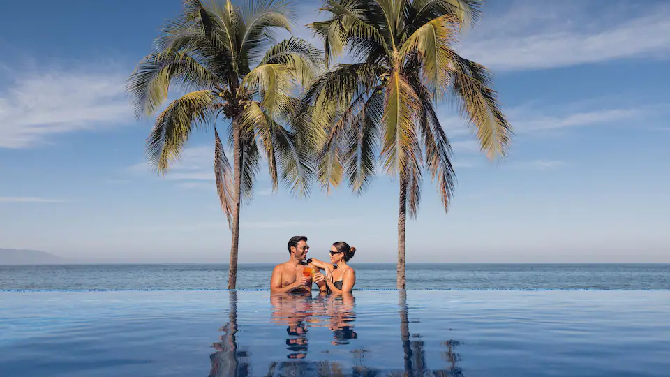 Couple enjoying cocktails in an infinity pool overlooking the Pacific Ocean at Hyatt Ziva Puerto Vallarta.