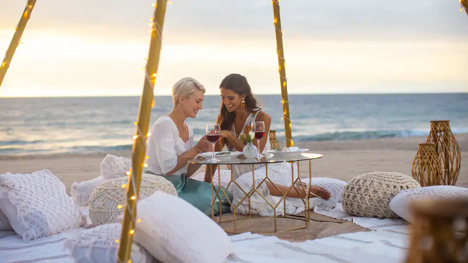 Two guests enjoying a luxury beachfront picnic setup at Hyatt Ziva Puerto Vallarta during sunset.