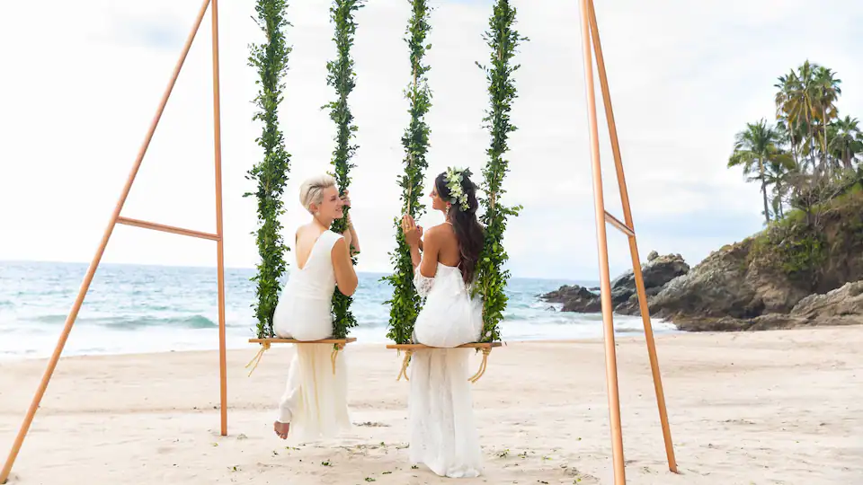 Newlyweds enjoying a decorative beach swing setup at Hyatt Ziva Puerto Vallarta with ocean views behind them.